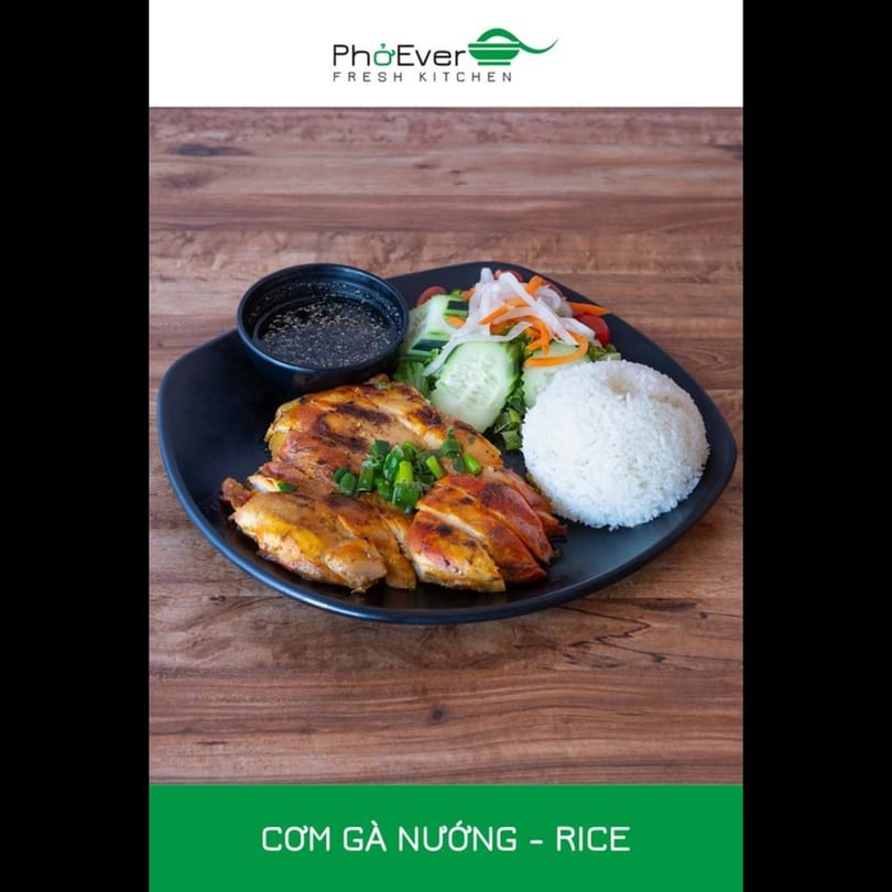 Grilled chicken with rice, salad, and dipping sauce on a black plate.
