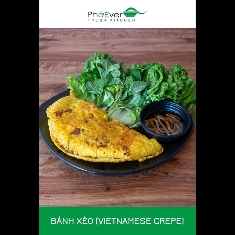 A golden Vietnamese crepe (Bánh Xèo) with fresh lettuce, mint, and dipping sauce on a wooden table.