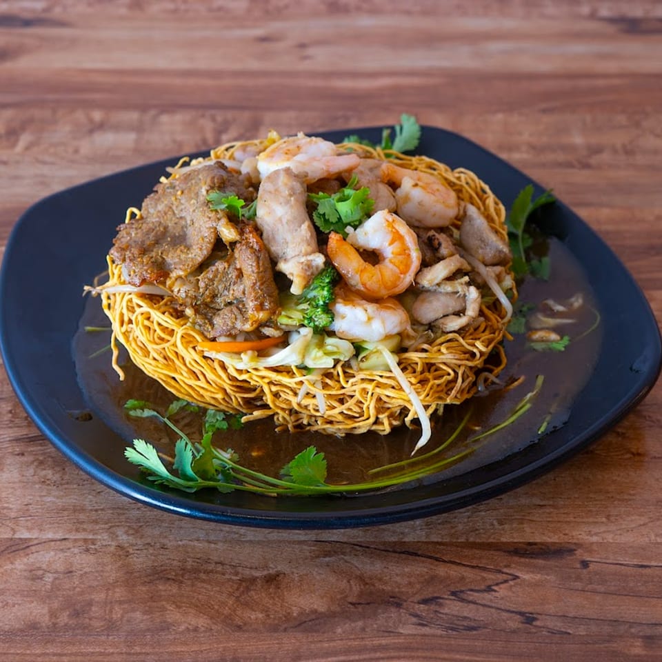 Crispy Vietnamese egg noodles with beef, shrimp, and vegetables in a savory sauce on a black plate.