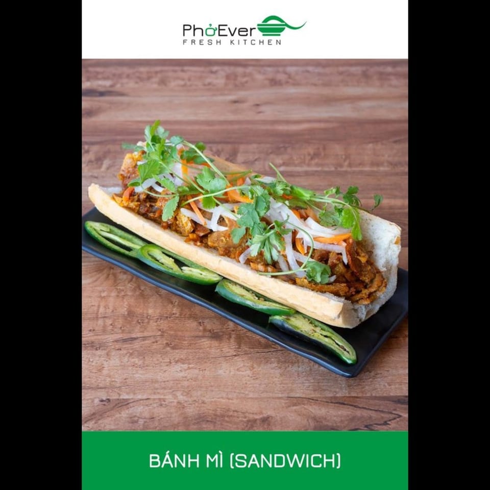 A Vietnamese Banh Mi sandwich with meat, pickled vegetables, and cilantro, served with jalapeños.