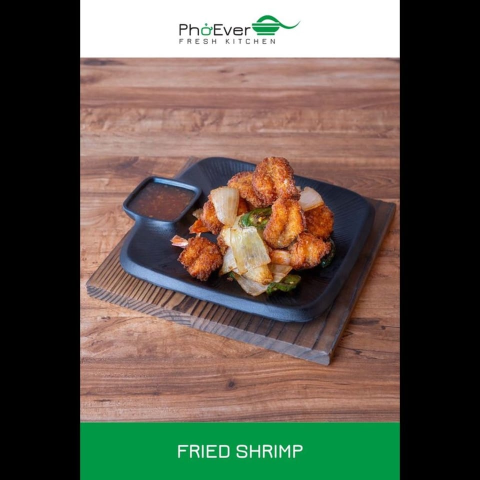 Fried shrimp with onions and green peppers, served with a dipping sauce on a black plate.