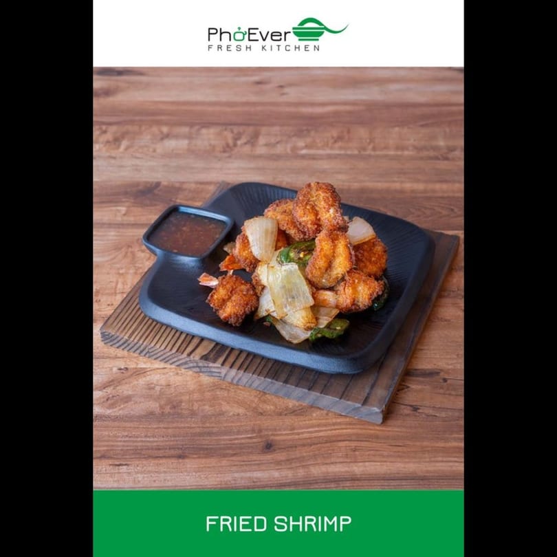 Fried shrimp with onions and green peppers, served with a dipping sauce on a black plate.
