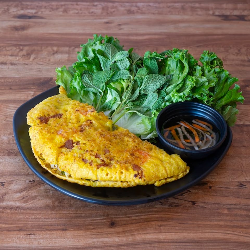 Vietnamese Banh Xeo, a crispy yellow crepe, with fresh lettuce, mint, and dipping sauce on a black plate.