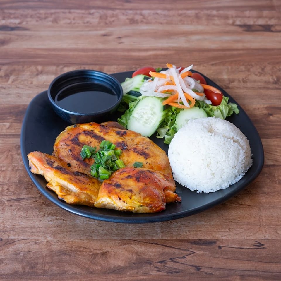 Grilled chicken with scallions, white rice, a side salad, and a bowl of sauce on a black plate.