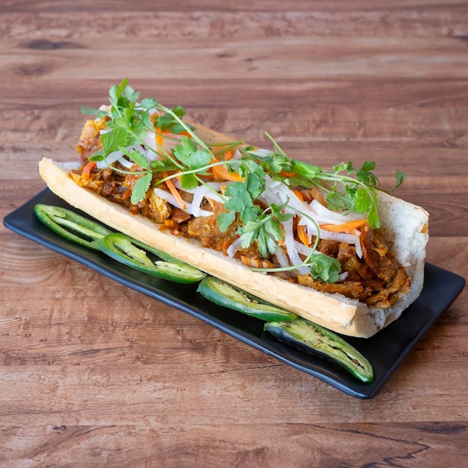 A Vietnamese Banh Mi sandwich with meat, pickled vegetables, cilantro, and sliced jalapeños on a black plate.