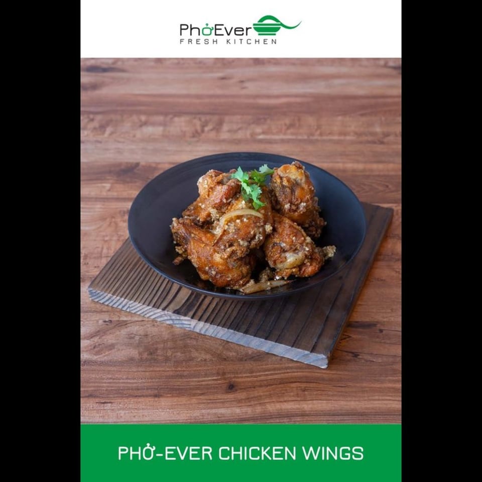 A black bowl of crispy Pho-Ever Chicken Wings, garnished with cilantro, on a wooden board.