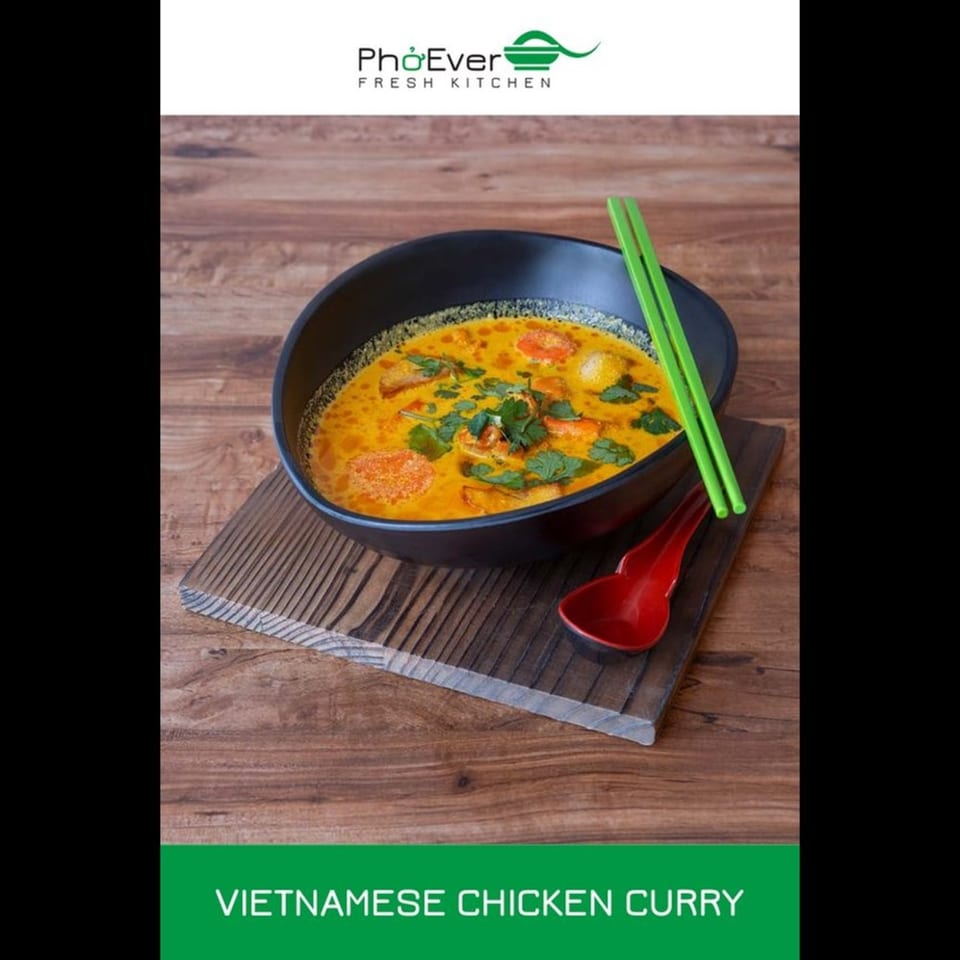 A black bowl of vibrant Vietnamese chicken curry with cilantro, green chopsticks, and a red spoon.